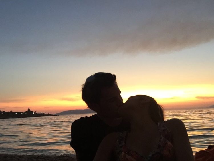 a couple kissing and hugging on a bridge at sunset