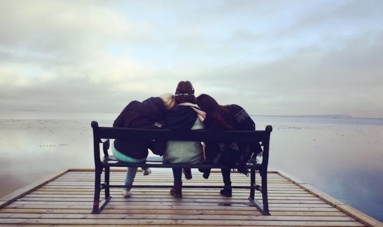 friends sitting on a bench at the end of a pier