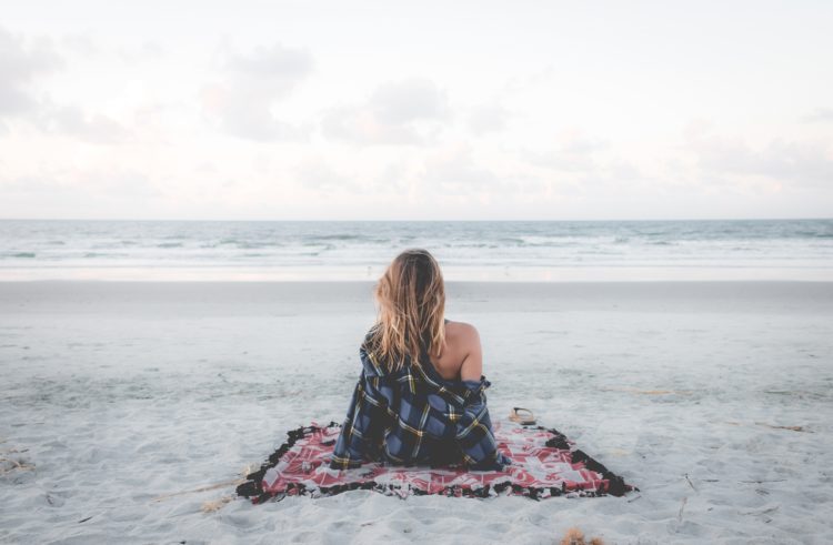 woman sitting on a blanket on the beach looking at the ocean