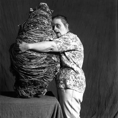 Black and white photo of artist Judith Scott, who has Down syndrome, hugging one of her fiber sculptures.
