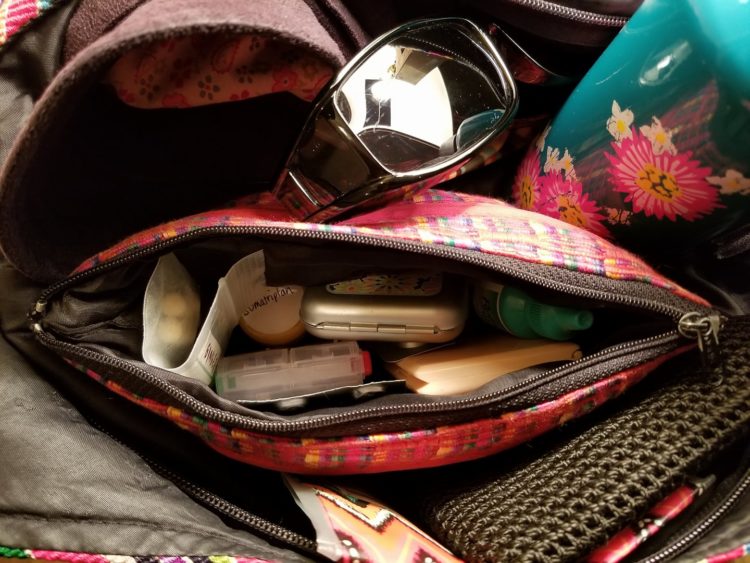 pink purse unzipped to show supplies, also sunglasses and water bottle