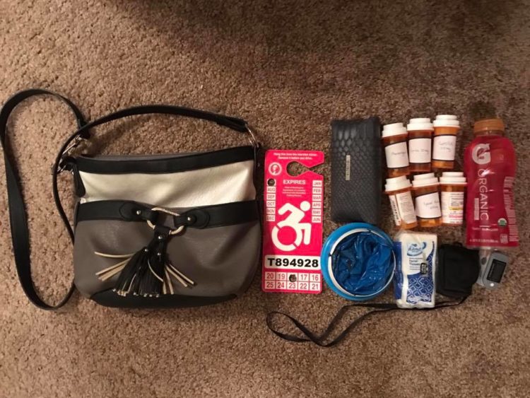 black purse with disabled pass, pills, gatorade tissues next to it
