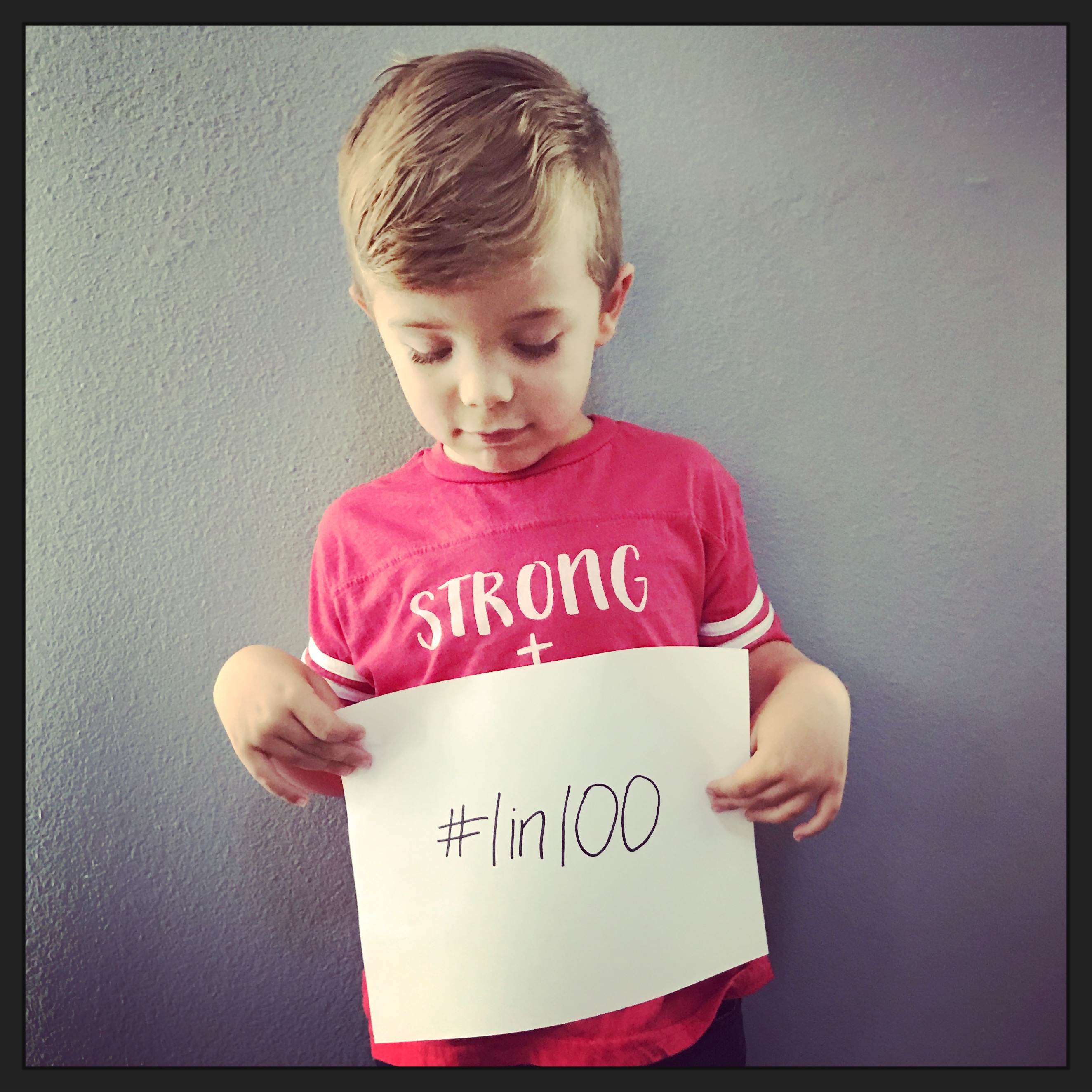 The author's son, holding a sign that says [hashtag] 1 in 100 