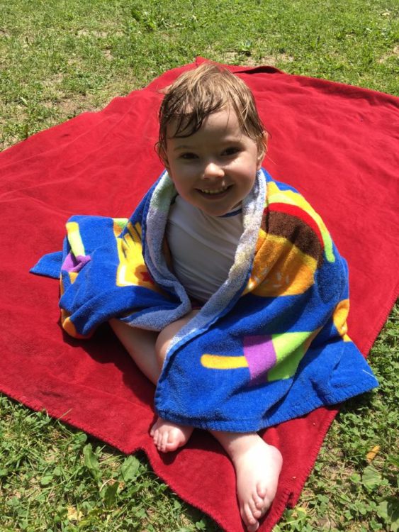 Boy sitting on blanket with towel around him after swimming
