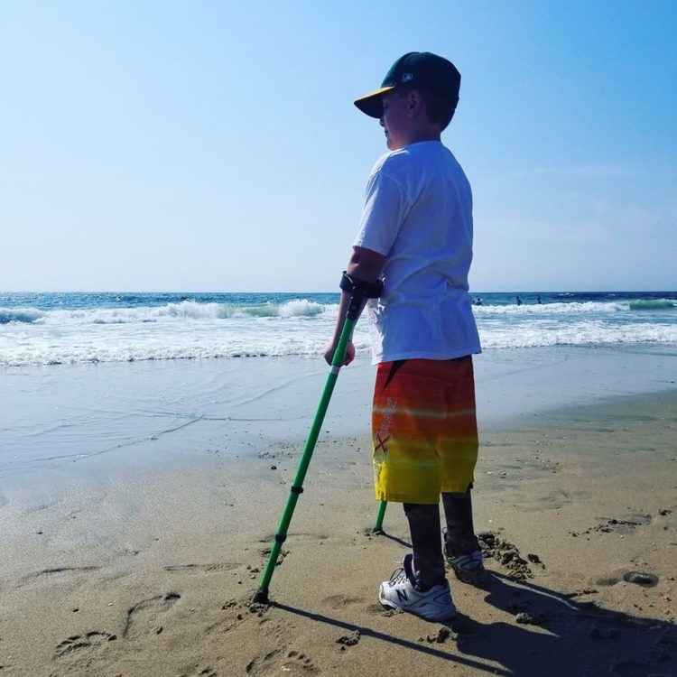 Boy standing by the ocean using crutches