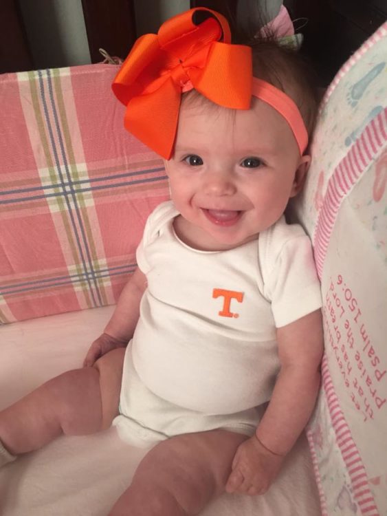 Baby girl with big orange bow sitting on a couch