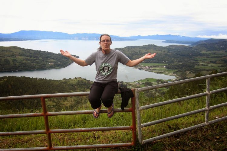 woman sitting on a fence overlooking a lake and mountains in indonesia