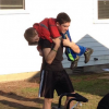 A teenage boy carrying his young brother on his shoulders