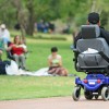 A person in their wheelchair at a park looking at other people