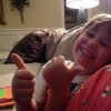 A small girl gives a thumbs up while seated on a couch