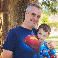 father and son in superman shirts hugging in park