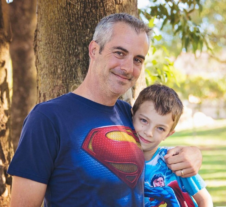 father and son in superman shirts hugging in park