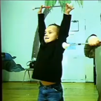 Two little boys holding sticks, one above his head and the other under his neck, as they stand in dance studio