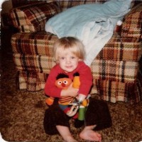 A young boy who is missing his lower forearm sits in front of the couch.