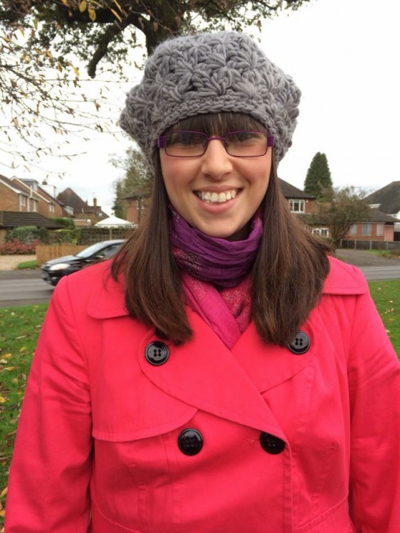 A photo of Sophie Webster outdoors wearing a red coat and gray knit hat