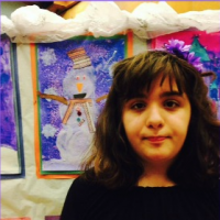 young girl standing in front of snowman paintings at school