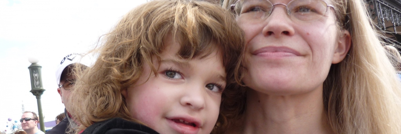 A mom looking up as her daughter sits in her lap and hugs her