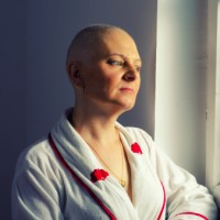 A bald female cancer patient looking out hospital window