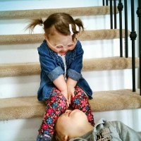 Young girl with Down syndrome smiling at her brother who is lying upside down on the stairs