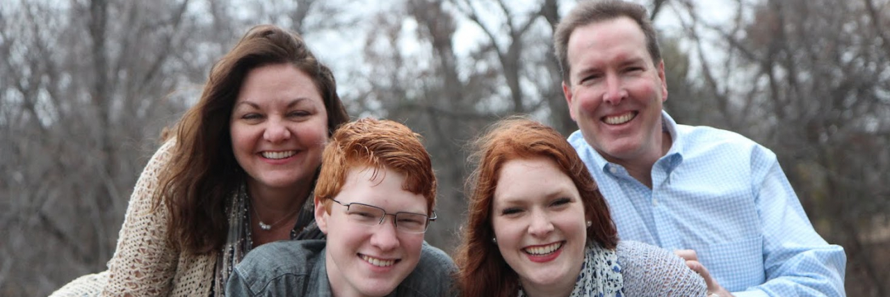 I Took This Photo for My Best Friend's Family. Then I Found Out Why. Photo of woman smiling with her family, including her husband and two children, posing outside