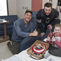 Chris Evans and Chris Pratt sitting smiling next to a boy in his hospital bed at Seattle Children's Hospital