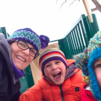 mom with two sons in winter clothes playing outside on a playground