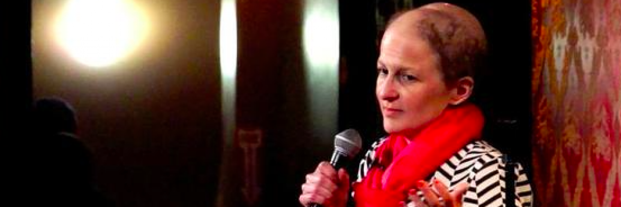 This Awesome Woman Is Making People Laugh About a Disease That's Not All That Funny Comedian Nicole Osborne on stage holding microphone during standup routine