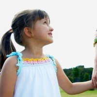 Woman holding daughter's (3-5) hand in park, girl smiling up at mother