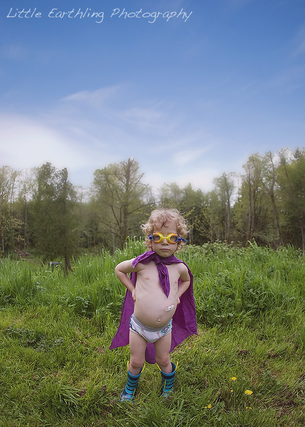 Apollo wearing purple cape and goggles, standing on the grass with trees in the background