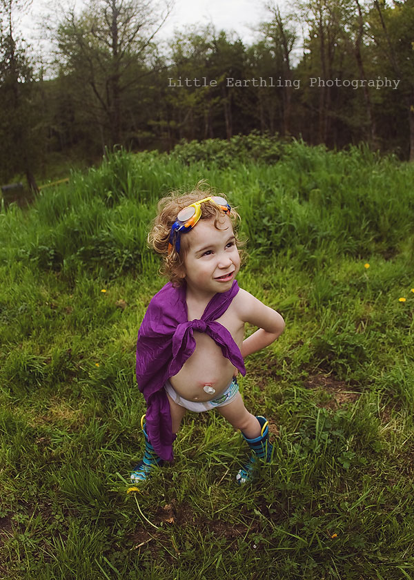 Apollo wearing purple cape and goggles, standing in the grass with trees in the background