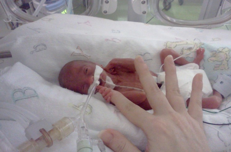 preemie baby holding an adult finger