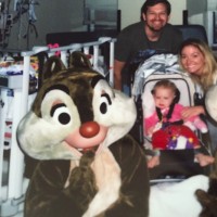 A dad, mom and daughter in stroller surrounded by Disney characters in costume