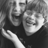 A laughing girl with her arms around her laughing younger brother in glasses