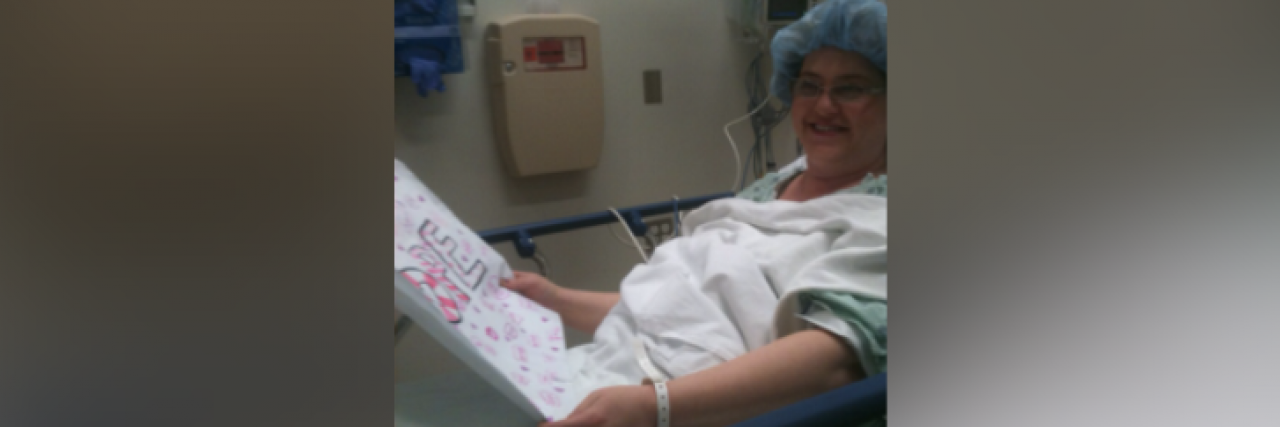 Woman in hospital bed holding a sign and smiling
