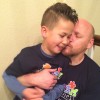 A dad kisses his son on the cheek as he sits on his lap