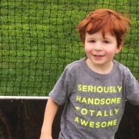 a red-headed small boy wearing a t-shirt that says, "Seriously Handsome. Totally Awesome," while standing in front of a soccer net