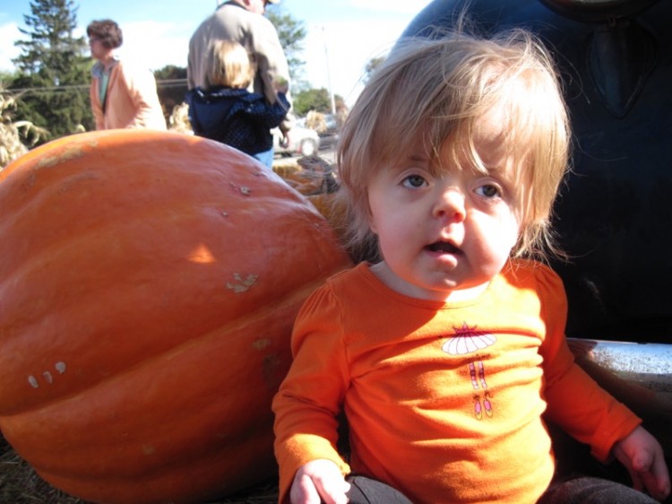 girl in orange shirt sitting next to a pumpkin