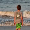 Boy in t-shirt and shorts standing near beach shore