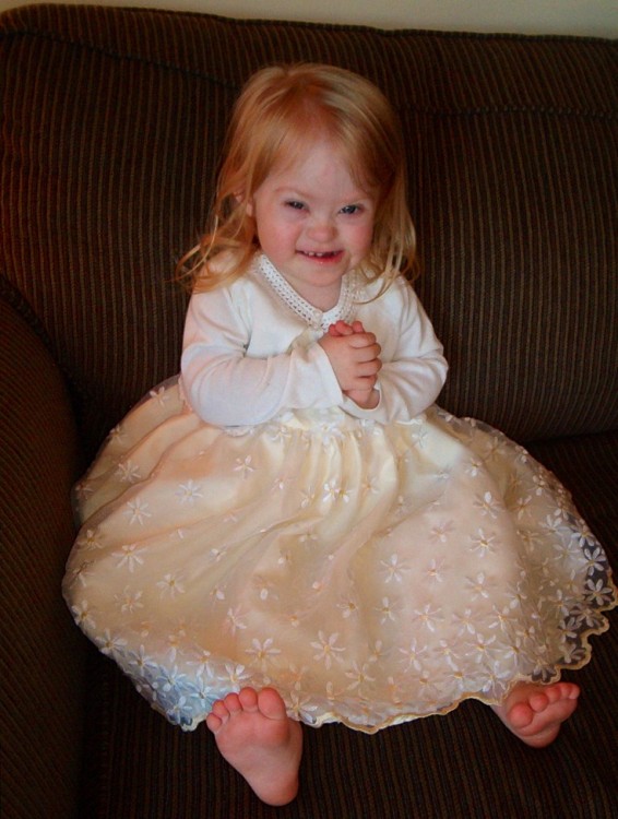A little girl with Down syndrome wearing a tan dress.