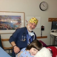 Doctor stands behind girl hugging her dog on hospital bed