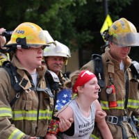 Two firefighters link arms with a woman as they walk.