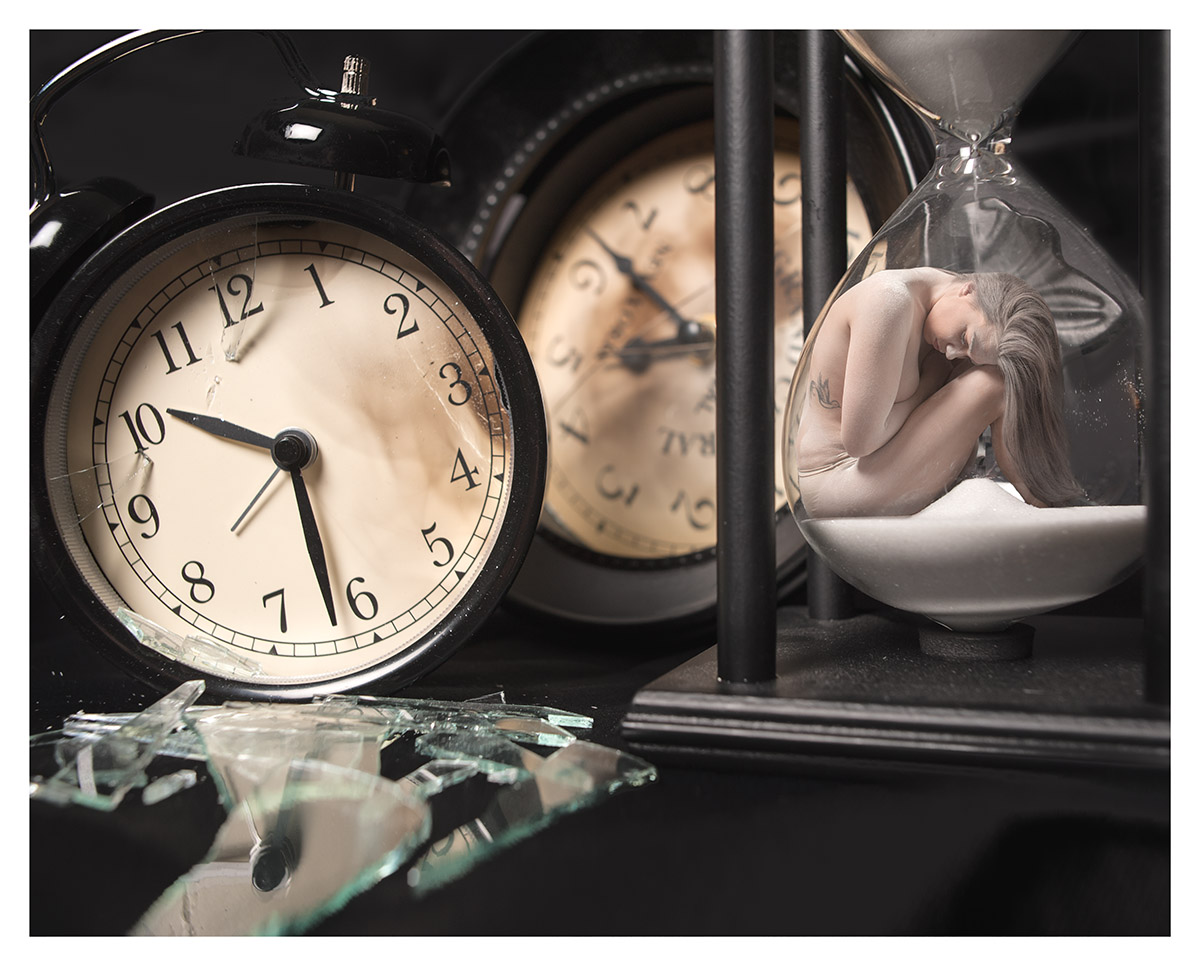 Two old clocks next to an hour glass. A woman is crouched inside the hour glass. 