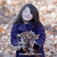 young girl poses outside wearing purple jacket and holding a handful of autumn leaves
