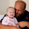 Dad pokes his daughter's belly as he sits on his lap