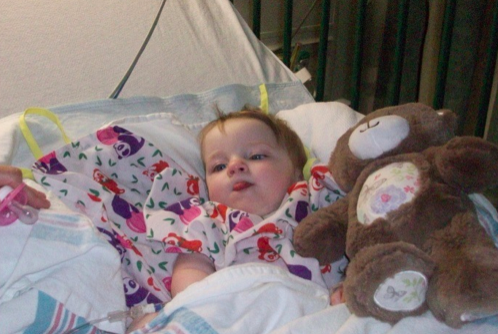 baby girl laying in a hospital bed next to a teddy bear
