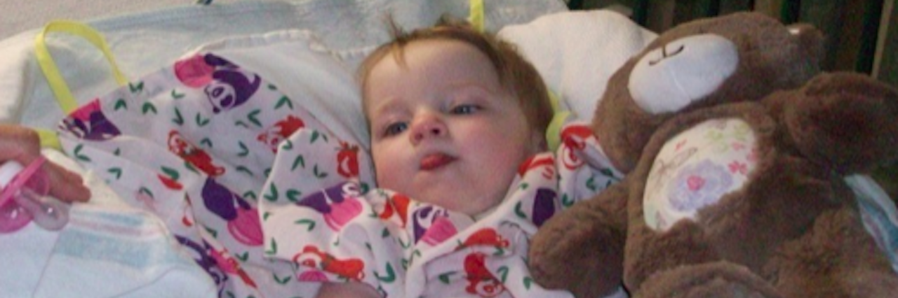 Opening Up About My Medically Fragile Daughter's Shortened Lifespan baby girl laying in a hospital bed next to a teddy bear