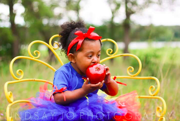 young girl wearing snow white costume and eating an apple