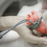 mother's hand holding feet of new born baby sick