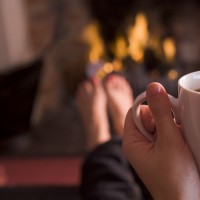 Feet warming at a fireplace with hands holding coffee