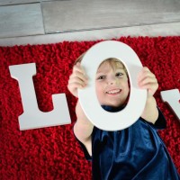 A little girl sticking her head through a cut-out that says, "LOVE," with her head in the "O"